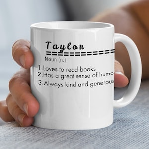 Può includere: Una tazza in ceramica bianca con un design nero che dice "Taylor" e definisce il nome come un sostantivo con tre caratteristiche: ama leggere libri, ha un grande senso dell'umorismo ed è sempre gentile e generoso.
