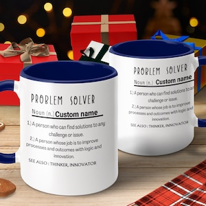 May include: White ceramic mug with a blue rim and handle. The mug features a black and white definition of "Problem Solver" with the word "Custom name" in place of the definition.