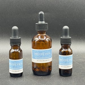May include: Three amber glass dropper bottles of varying sizes. Each bottle has a black dropper top and a light blue label with the word "PROTECTION" and the text "NOT FOR CONSUMPTION". The bottles are arranged against a dark background.