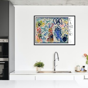 May include: A framed abstract painting of a colourful Easter scene with a bunny, flowers, and the word "EASTER" in black text. The painting is in a black frame and is hanging on a white wall in a kitchen.