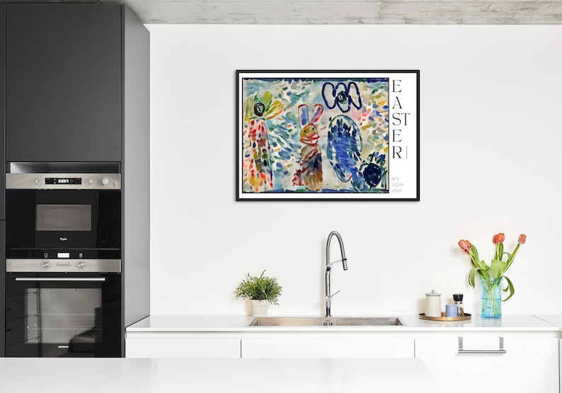 May include: A framed abstract painting of a colourful Easter scene with a bunny, flowers, and the word "EASTER" in black text. The painting is in a black frame and is hanging on a white wall in a kitchen.