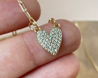 May include: A gold chain necklace with a heart-shaped pendant covered in small clear cubic zirconia stones.
