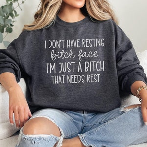 May include: Dark gray sweatshirt with the text "I DON'T HAVE RESTING bitch face I'M JUST A BITCH THAT NEEDS REST" in white. The sweatshirt is a crew neck style and is made of a soft material.