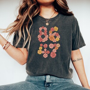 May include: A dark gray t-shirt with a floral design that spells out "86 & 17".