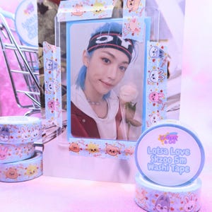 May include: A photo card of a person with blue hair and a headband, holding a rose, is displayed with decorative washi tape. The tape features cartoon animal designs and the text "Lotsa Love Skzoo 5m Washi Tape."