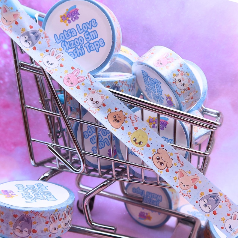 May include: A collection of light blue washi tape rolls with cartoon animal designs and the text "Lotsa Love Skzoo 5m Washi Tape." The tape features illustrations of a rabbit, bear, fox, and other characters. The rolls are in a miniature shopping cart.