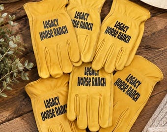 May include: A collection of five yellow leather work gloves arranged in a group. Each glove features the black printed text Legacy Horse Ranch on the back of the hand. The gloves have a standard five-finger design with a flared wrist opening.