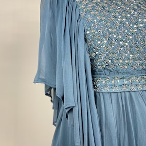 May include: A light blue formal dress with intricate beadwork and sequin embellishments. The bodice features a detailed pattern, and the sleeves are made of flowing, sheer fabric. The dress has a cinched waist and a flowing skirt, ideal for special occasions.