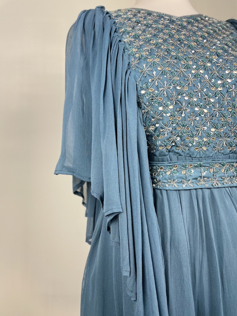 May include: A light blue formal dress with intricate beadwork and sequin embellishments. The bodice features a detailed pattern, and the sleeves are made of flowing, sheer fabric. The dress has a cinched waist and a flowing skirt, ideal for special occasions.