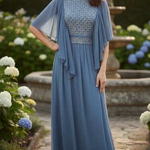 May include: A long, flowing, blue dress with a beaded bodice and a matching cape. The dress has a cinched waist and a floor-length skirt. The model is in a garden with a fountain in the background.