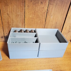 Könnte beinhalten: Eine graue Plastik-Aufbewahrungsbox mit zwei Fächern. Das obere Fach hat drei Reihen kleiner Metallringe und das untere Fach enthält eine Sammlung kleiner Schrauben.