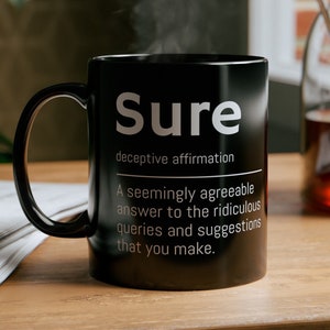 May include: Black coffee mug with white text that reads "Sure" and a definition of the word. The definition reads "deceptive affirmation. A seemingly agreeable answer to the ridiculous queries and suggestions that you make."