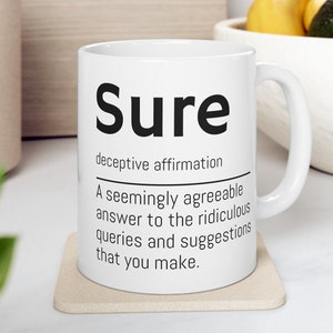 May include: White ceramic mug with a black design that says "Sure" and defines it as a "deceptive affirmation". The definition continues, "A seemingly agreeable answer to the ridiculous queries and suggestions that you make."