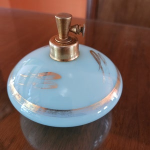 May include: A light blue glass atomizer bottle with a gold top and gold accents. The bottle has a delicate design of gold lines and a gold band around the bottom.