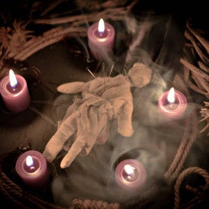 Puede incluir: Una muñeca vudú con alfileres clavados en ella, rodeada de cinco velas moradas, algunas de las cuales están encendidas, sobre un fondo oscuro.