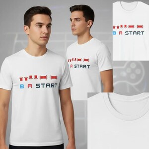 May include: A white short-sleeved t-shirt featuring a graphic print of red directional arrows and the text B A START in blue and black. The design mimics a classic video game controller input sequence on the chest of the garment.