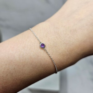 May include: A delicate silver chain bracelet with a single purple gemstone.