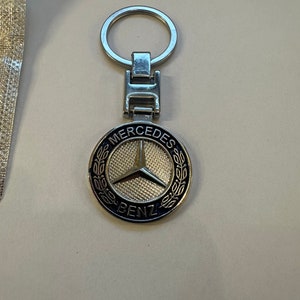 May include: A silver key chain with a black and silver Mercedes-Benz logo charm. The logo features a three-pointed star and the words "Mercedes-Benz".