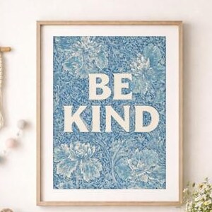 Pode incluir: Uma impressão emoldurada com as palavras "BE KIND" em letras brancas grandes sobre um fundo floral azul. A impressão é exibida acima de uma cômoda de madeira com um ursinho de pelúcia, um arco-íris e outros itens decorativos.