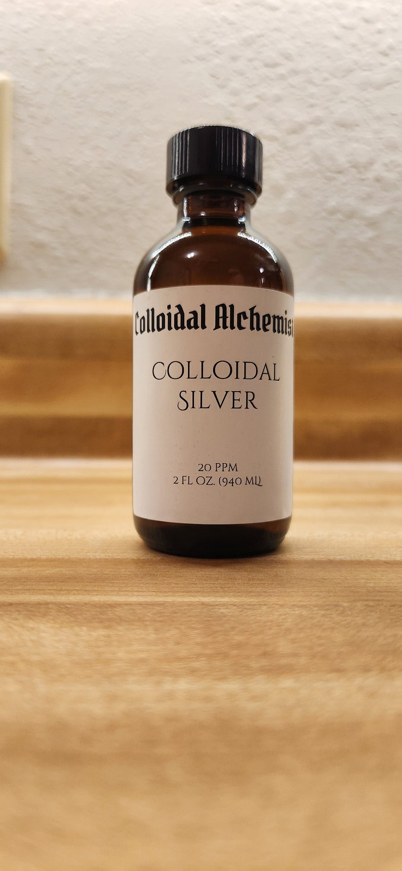 May include: A brown glass bottle with a black cap, labeled "Colloidal Alchemist Colloidal Silver 20 PPM 2 FL OZ. (940 ML)"