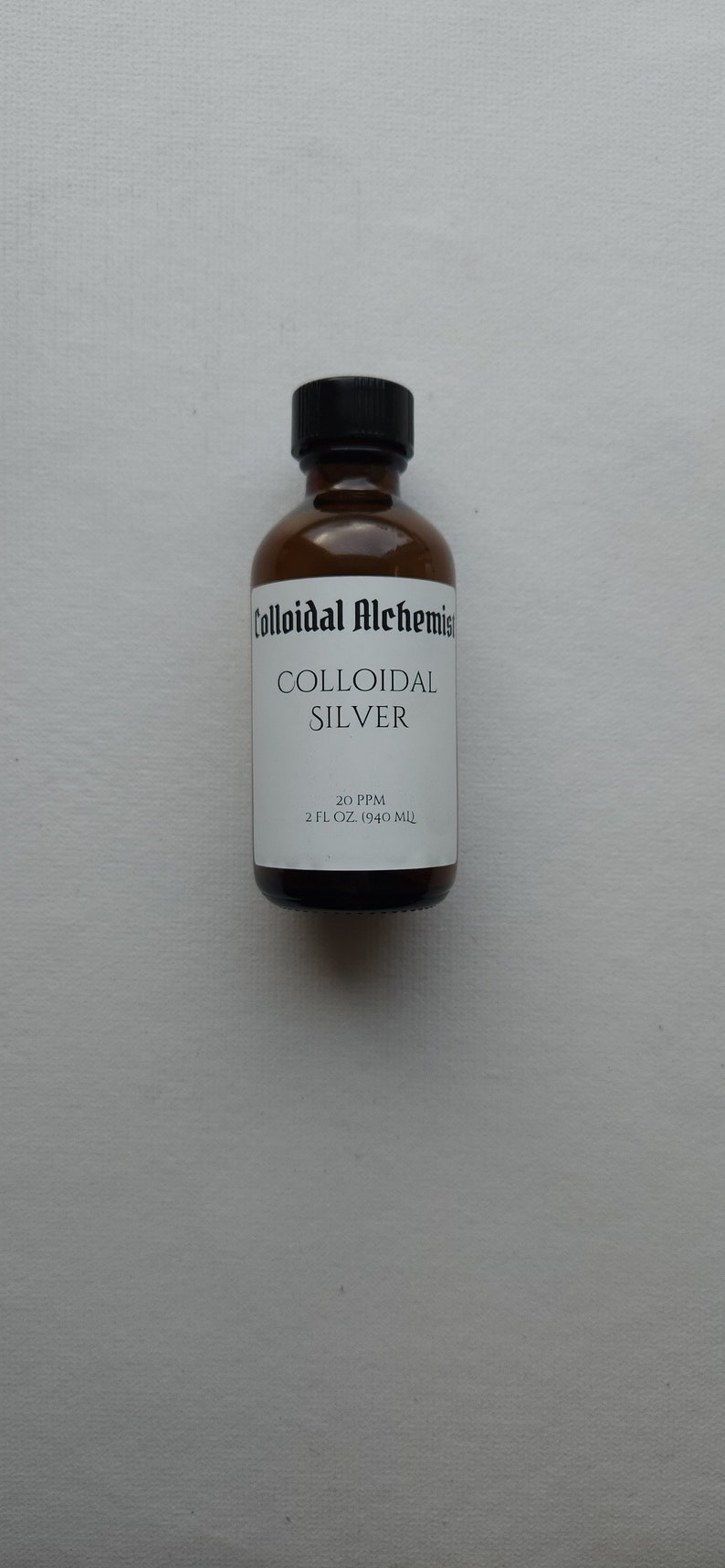 May include: A brown glass bottle with a black cap, labeled "Colloidal Alchemist Colloidal Silver 20 PPM 2 FL OZ. (59.14 ML)"