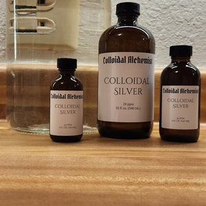 May include: Three amber glass bottles of colloidal silver, labeled "Colloidal Alchemist" with different sizes: 2 fl oz, 4 fl oz, and 16 fl oz. The bottles are on a wooden surface.