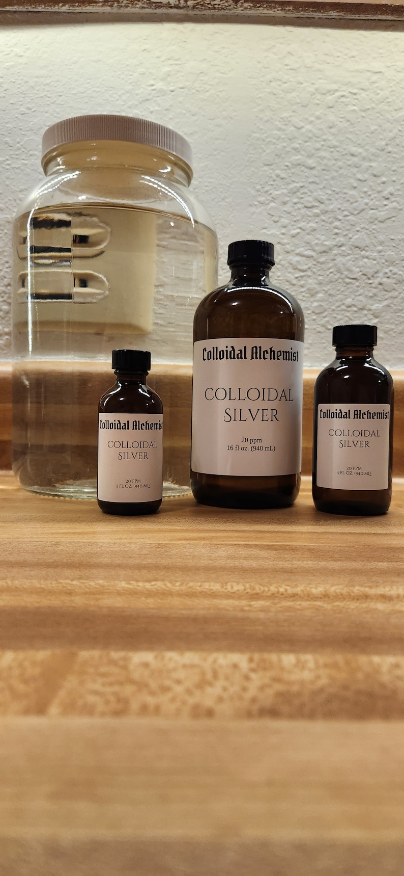 May include: Three amber glass bottles of colloidal silver, labeled "Colloidal Alchemist" with different sizes: 2 fl oz, 4 fl oz, and 16 fl oz. The bottles are on a wooden surface.