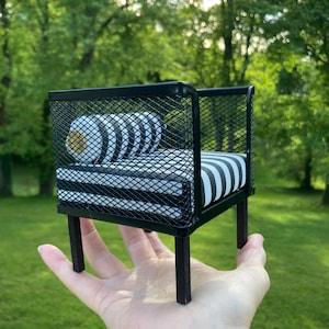 May include: A miniature black metal chair with a black and white striped cushion. The chair is sitting on a hand.
