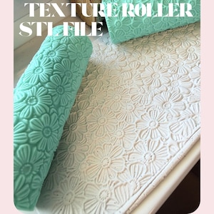 Può includere: Primo piano di un rullo per texture turchese con un motivo a margherita, accanto a una superficie con lo stesso disegno a rilievo. Le parole "TEXTURE ROLLER STL FILE" sono stampate in bianco nella parte superiore dell'immagine.