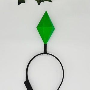 May include: A black headband with a green diamond-shaped topper. The headband is made of plastic and the topper is made of a soft, pliable material.