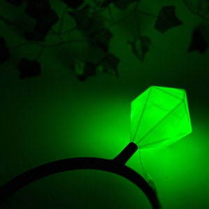 May include: A green glow-in-the-dark diamond ring headband. The headband is black and the diamond is a bright green.