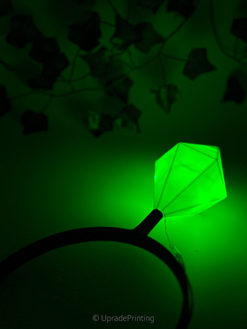 May include: A green glow-in-the-dark diamond ring headband. The headband is black and the diamond is a bright green.