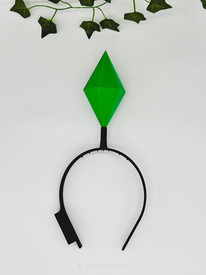 May include: A black headband with a green diamond-shaped topper. The headband is made of plastic and the topper is made of a soft, pliable material.