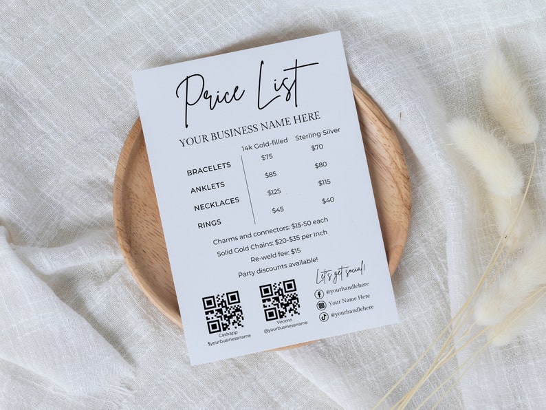 May include: A white price list on a wooden plate, featuring the text "Price List" and "YOUR BUSINESS NAME HERE." It lists prices for bracelets, anklets, necklaces, and rings in both 14k gold-filled and sterling silver. Includes QR codes and social media handles.