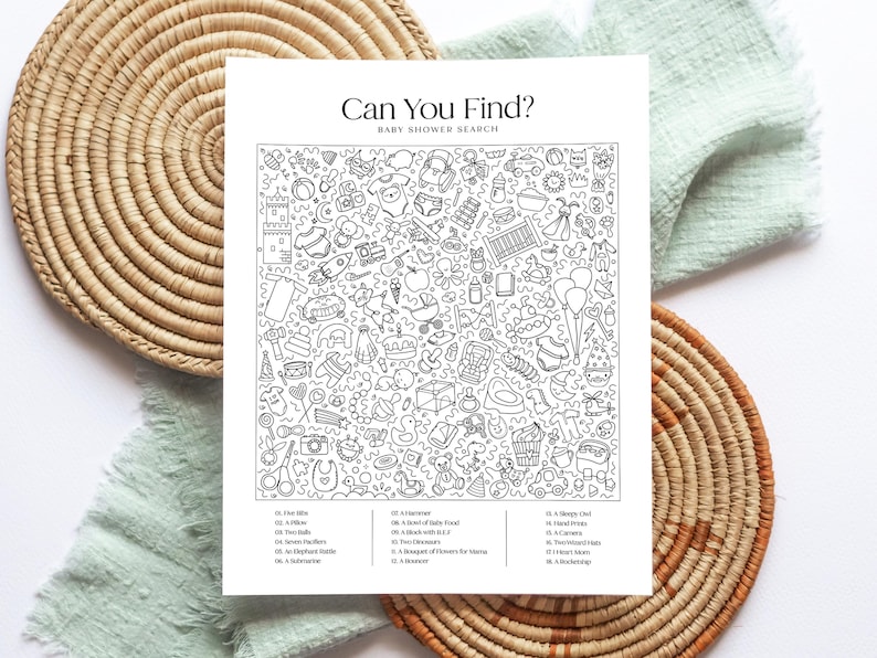 May include: Black and white baby shower search game with the text "Can You Find?" and a list of items to find. The game is surrounded by woven placemats and a green cloth.