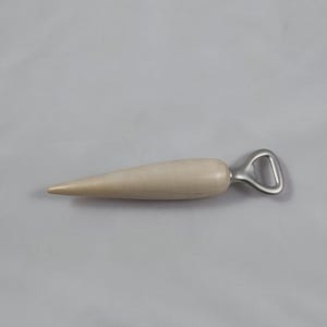 Puede incluir: Un abridor de botellas de madera con un mango cónico de color claro y un abridor de metal plateado. El mango es liso y parece estar hecho de madera clara. El abridor tiene un diseño simple y funcional.