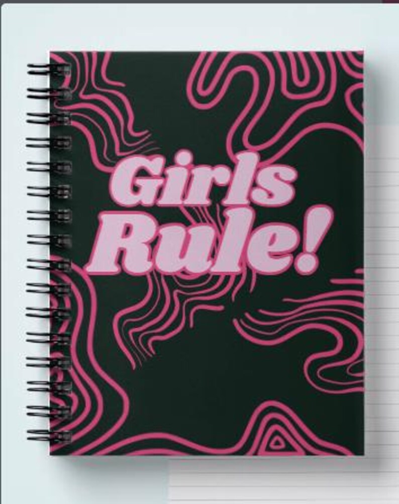 May include: A black spiral notebook with a pink and black abstract design. The notebook has the text "Girls Rule!" in pink letters.