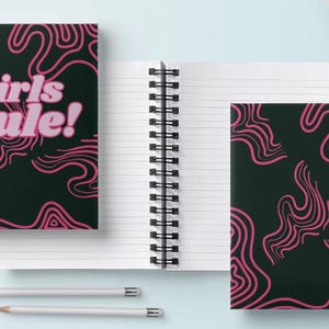 May include: Two spiral bound notebooks with black covers and pink abstract line designs. One notebook has the text "Girls Rule!" in pink letters.