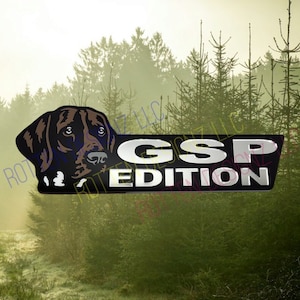 Peut inclure: Un autocollant noir et argent avec la tête d'un Braque allemand à poil court et le texte "GSP EDITION". L'autocollant est placé sur un fond flou d'une forêt.