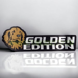 May include: A black and silver license plate frame with a golden retriever dog illustration and the text "GOLDEN EDITION".