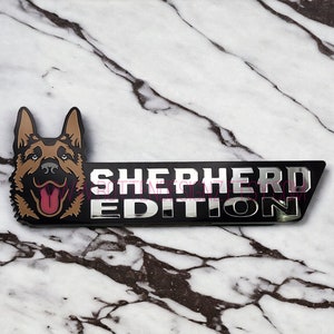 以下が含まれることがあります： ドイツシェパードの犬の頭と「SHEPHERD EDITION」の文字が書かれた黒と銀の金属製のエンブレムです。