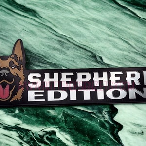 以下が含まれることがあります： ジャーマンシェパードの犬の頭と「SHEPHERD EDITION」の文字が書かれた黒と銀の金属製のエンブレムです。