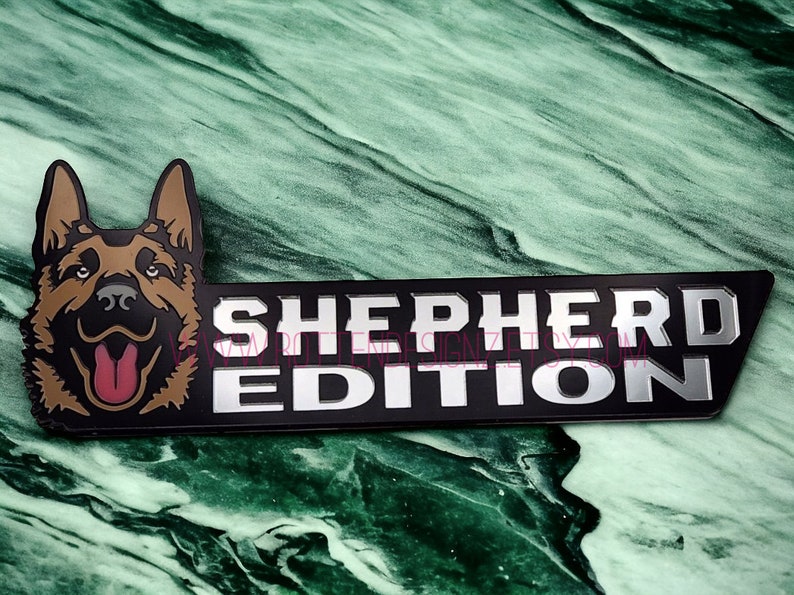 以下が含まれることがあります： ジャーマンシェパードの犬の頭と「SHEPHERD EDITION」の文字が書かれた黒と銀の金属製のエンブレムです。