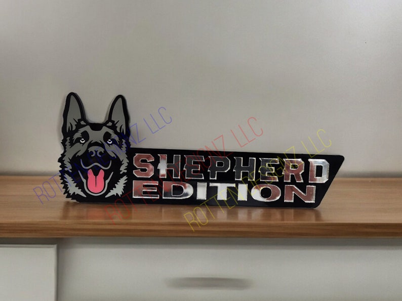 以下が含まれることがあります： ジャーマンシェパードの犬の頭と「SHEPHERD EDITION」の文字が書かれた黒と銀の金属製のエンブレムです。