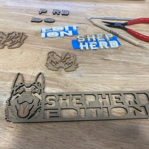 以下が含まれることがあります： 「SHEPHERD EDITION」という文字が大きく太字で書かれた木製の看板。看板の左側には、ジャーマンシェパードの頭部の切り抜きがある。