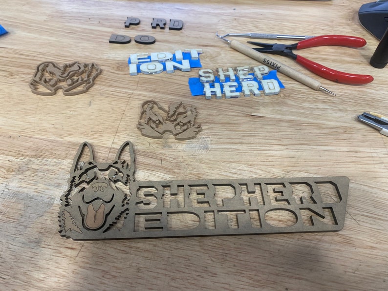 以下が含まれることがあります： 「SHEPHERD EDITION」という文字が大きく太字で書かれた木製の看板。看板の左側には、ジャーマンシェパードの頭部の切り抜きがある。