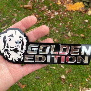 May include: A black and silver car emblem with a white silhouette of a golden retriever's head and the text "GOLDEN EDITION".