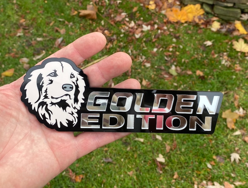 May include: A black and silver car emblem with a white silhouette of a golden retriever's head and the text "GOLDEN EDITION".