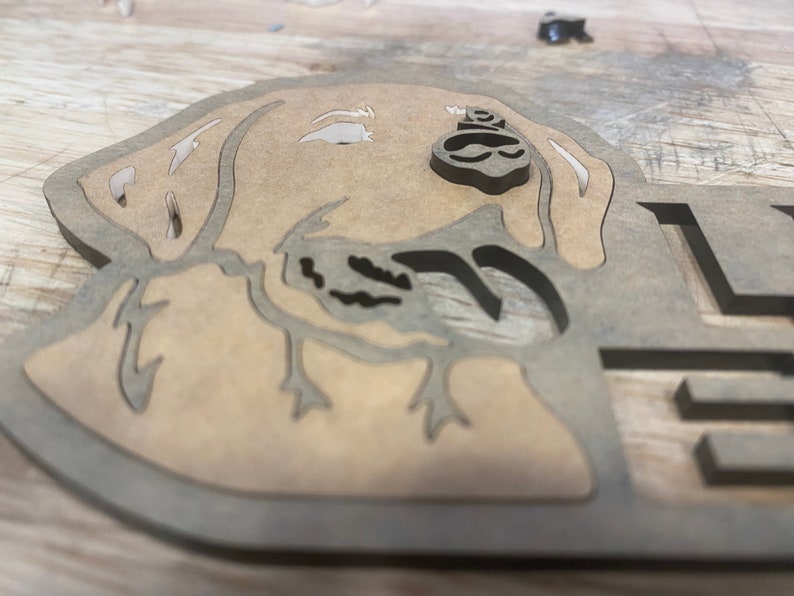 May include: A wooden cutout of a dog's head, with a brown stain finish. The dog's head is facing to the right, and the cutout is detailed with the dog's ears, nose, and mouth.