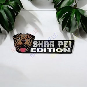 May include: Black and silver car emblem with a cartoon Shar Pei dog with a pink heart. The text reads "Shar Pei Edition".